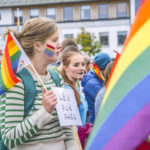 Folk i paraden med regnbueflagg. kvinne holder "lev for faen"-plakat